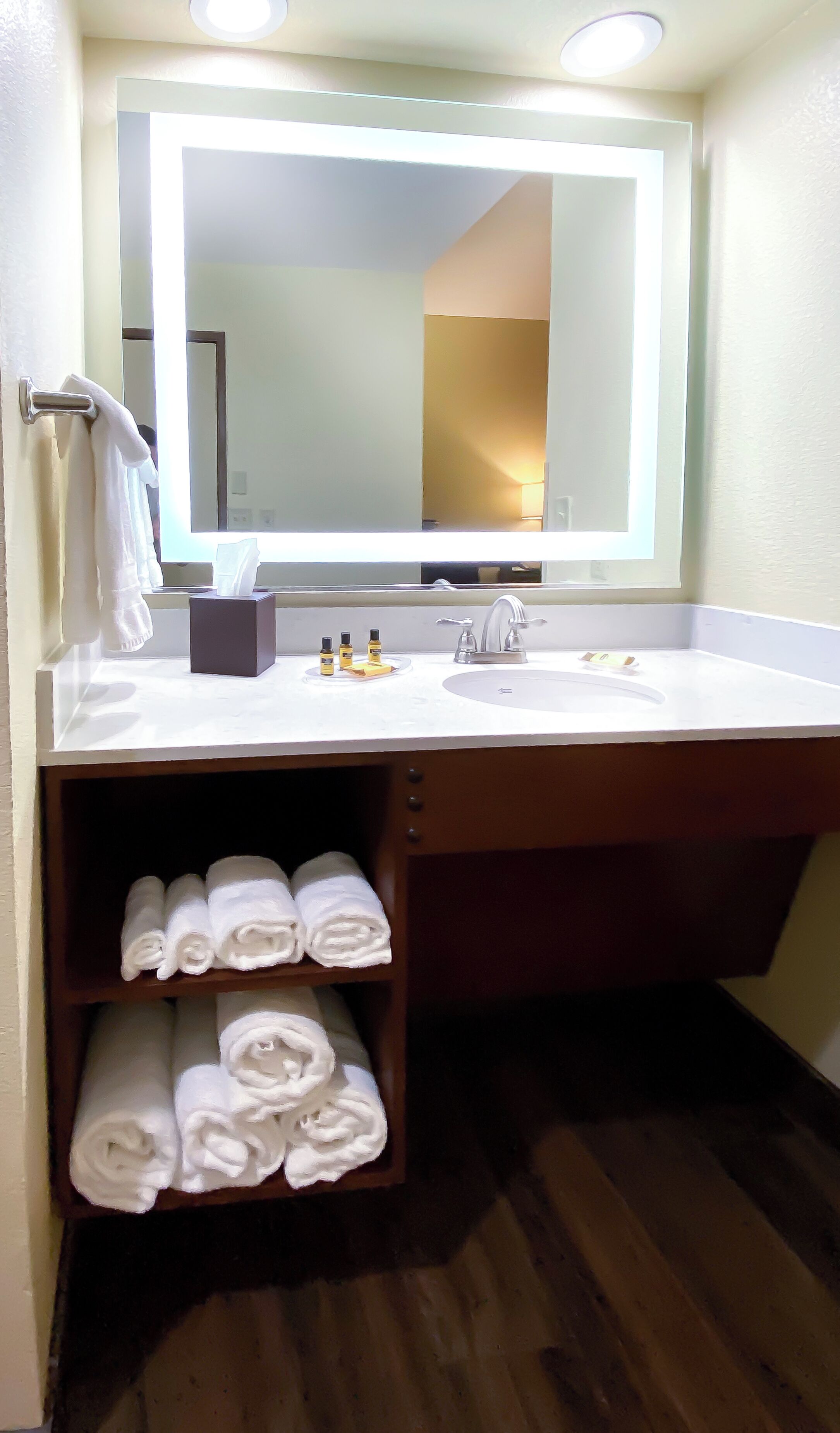 A bathroom with a large mirror, a white sink, and a shelf with neatly folded towels.