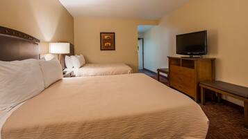 A hotel room with two beds, a TV on a wooden stand, a desk with a chair, and a framed picture on the wall.