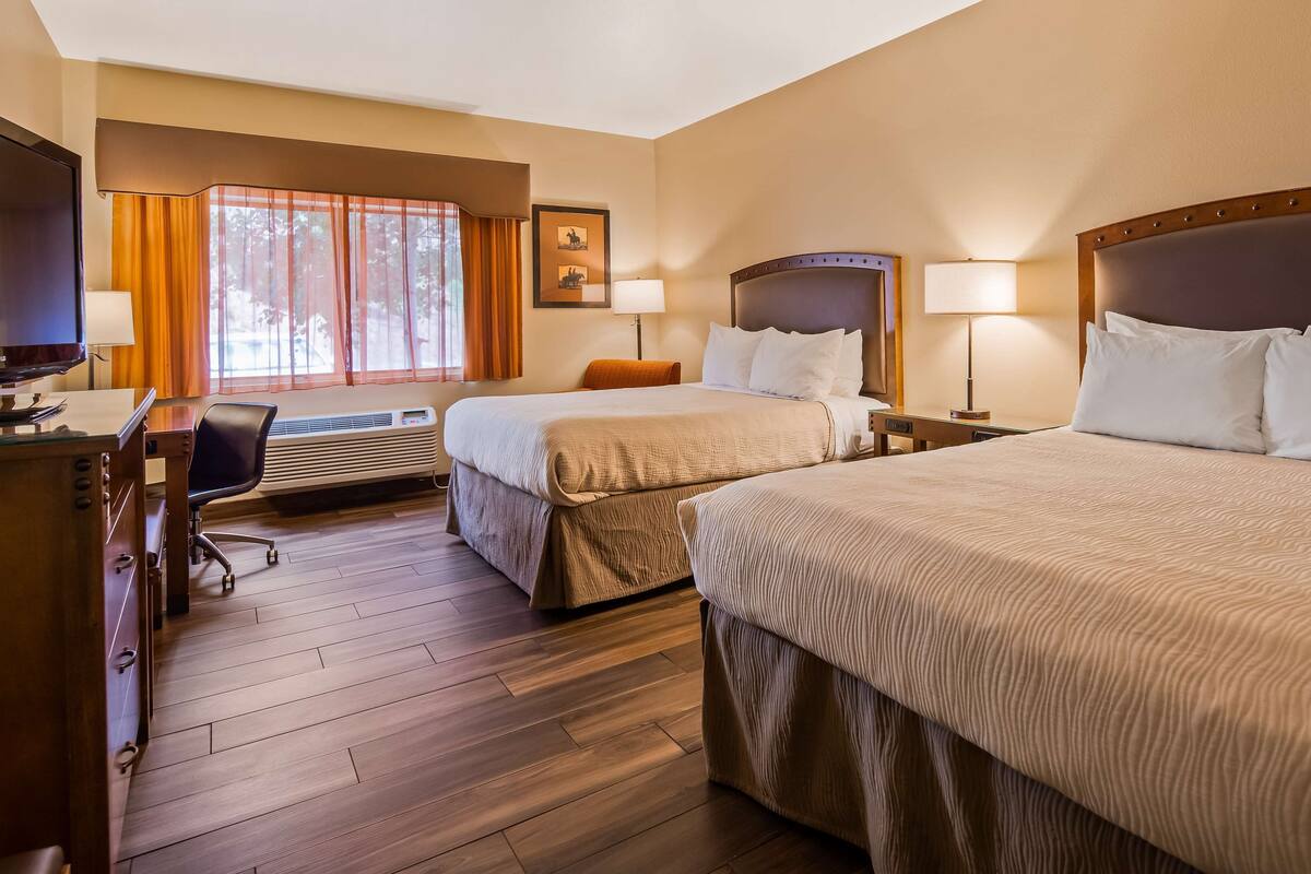 A hotel room with two beds, a desk, a chair, a television, and a window with curtains.