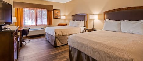 A hotel room with two beds, a desk, a chair, a television, and a window with curtains.