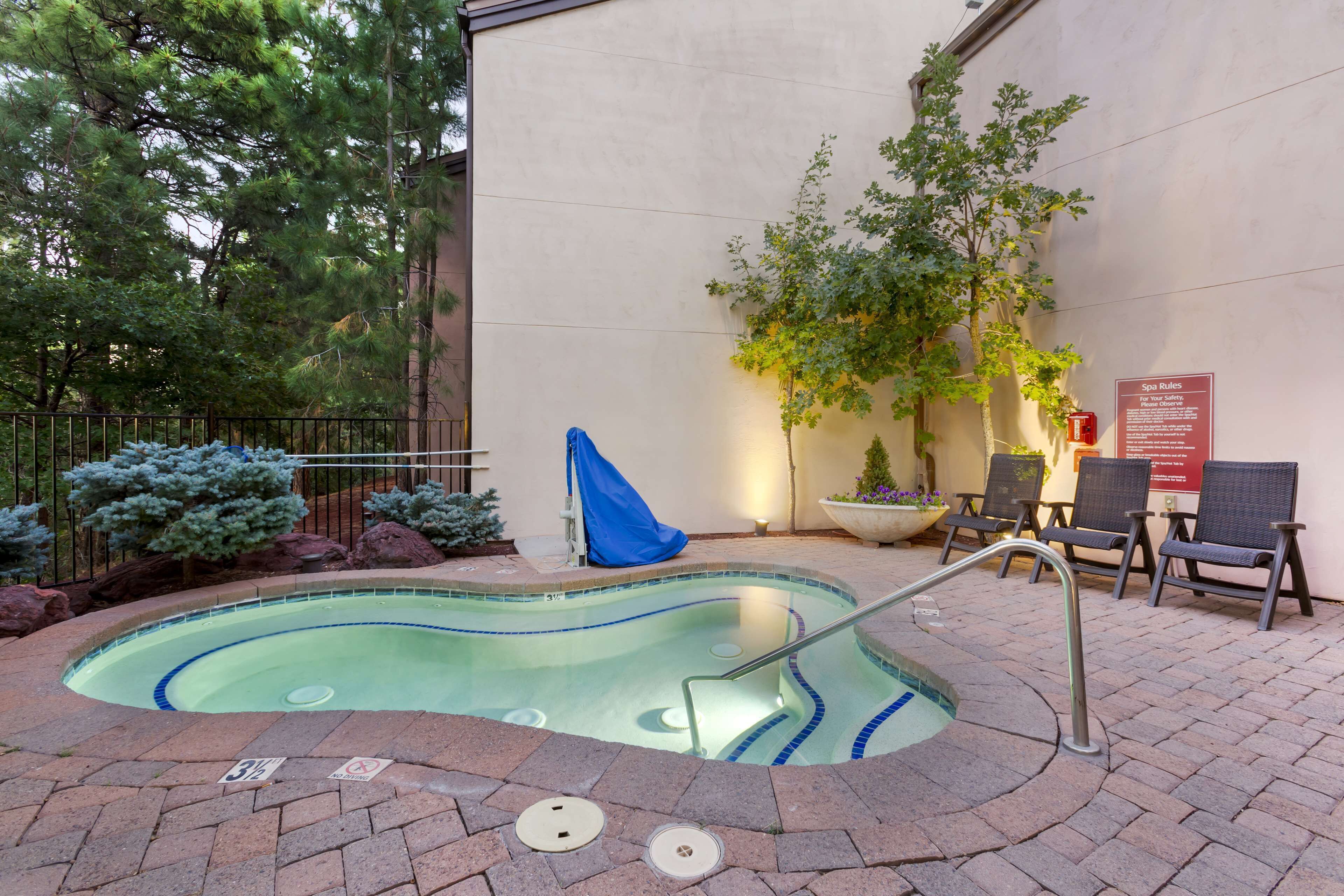 A small outdoor pool with a metal ladder, surrounded by a brick patio. There are lounge chairs and a sign indicating spa rules.