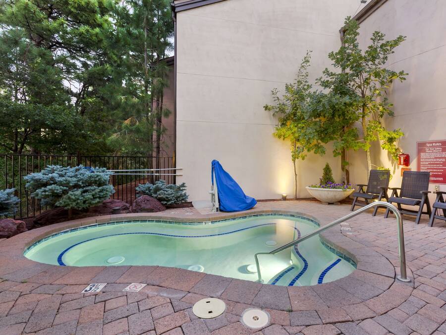 A small outdoor pool with a metal ladder, surrounded by a brick patio. There are lounge chairs and a sign indicating spa rules.