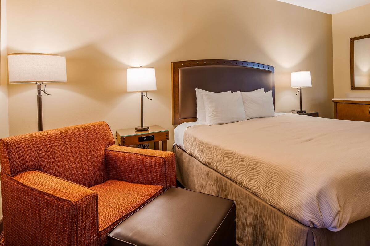 A hotel room with a bed, two bedside lamps, a chair, and a small table.