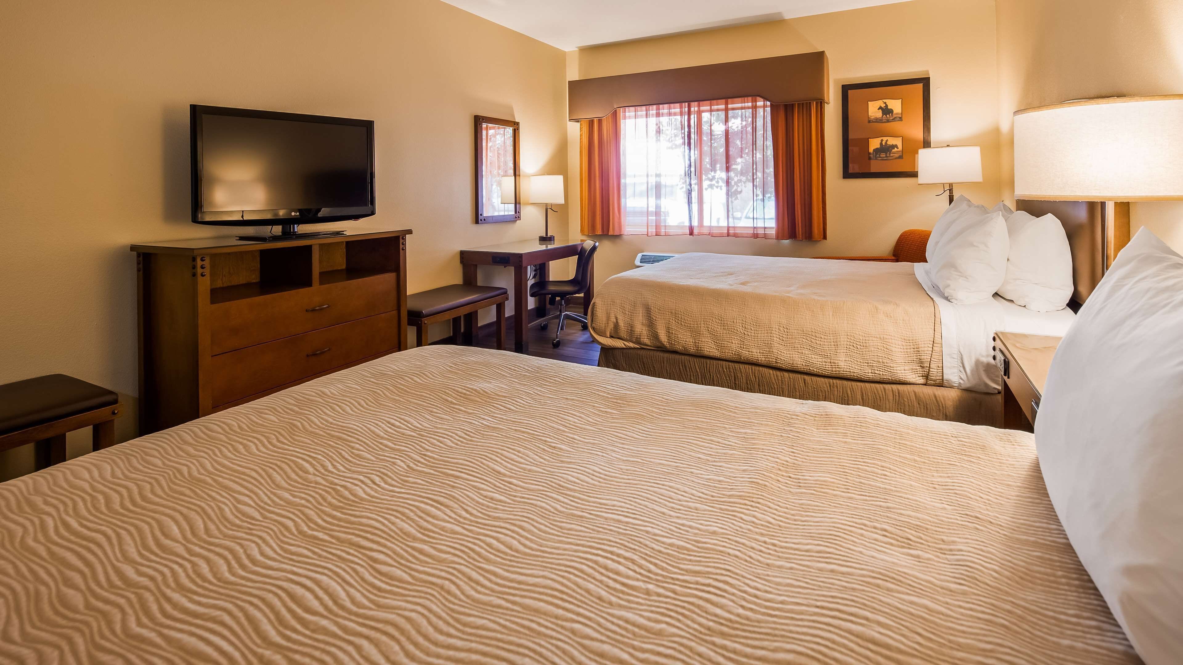 A hotel room with two beds, a desk, a television, and a window with curtains.