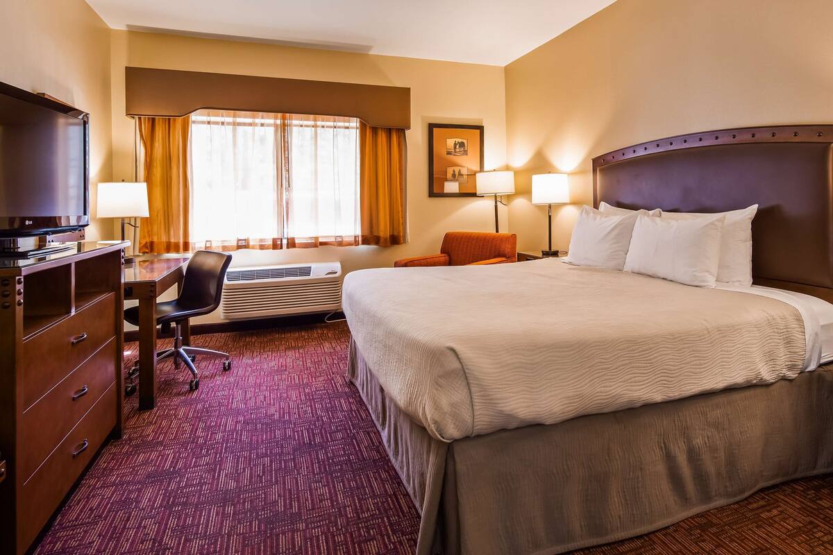 A hotel room with a bed, desk, chair, TV, and a large window with curtains.