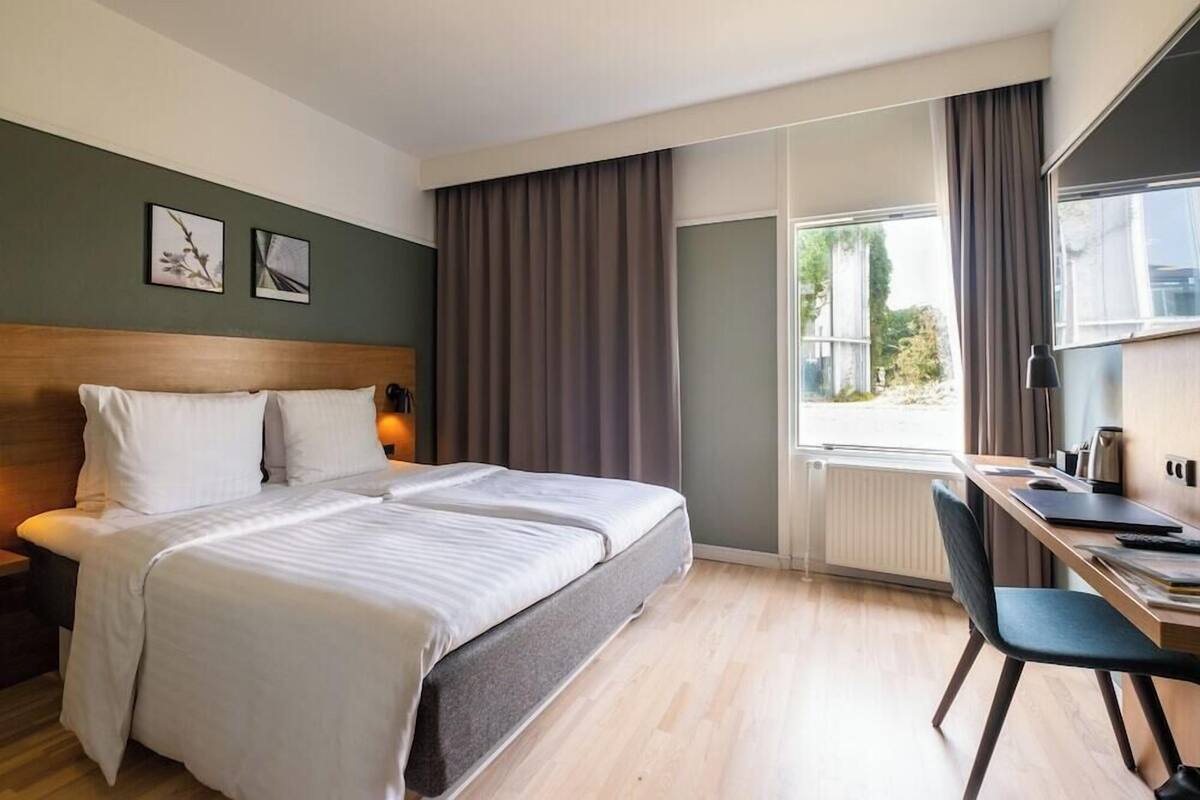 Et hotelværelse med en seng, et skrivebord, en stol og udsigt til det fri.
