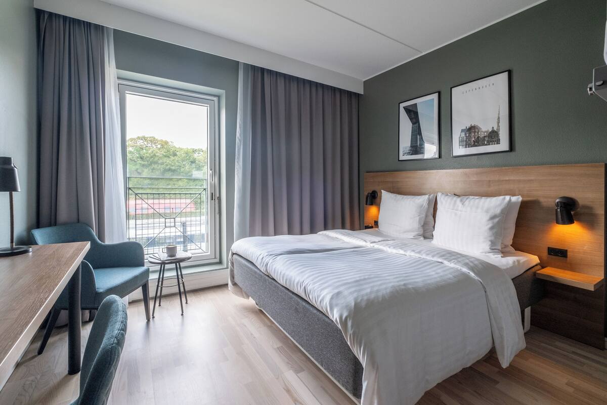 Et hotelværelse med en stor seng, et skrivebord, en stol og udsigt til det fri.