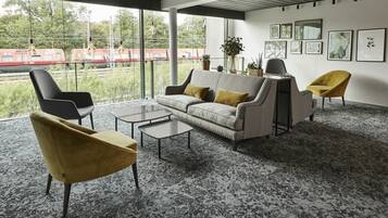 Ett modernt vardagsrum med en soffa, två fåtöljer och ett soffbord. Det finns stora fönster med utsikt över ett tåg som passerar.