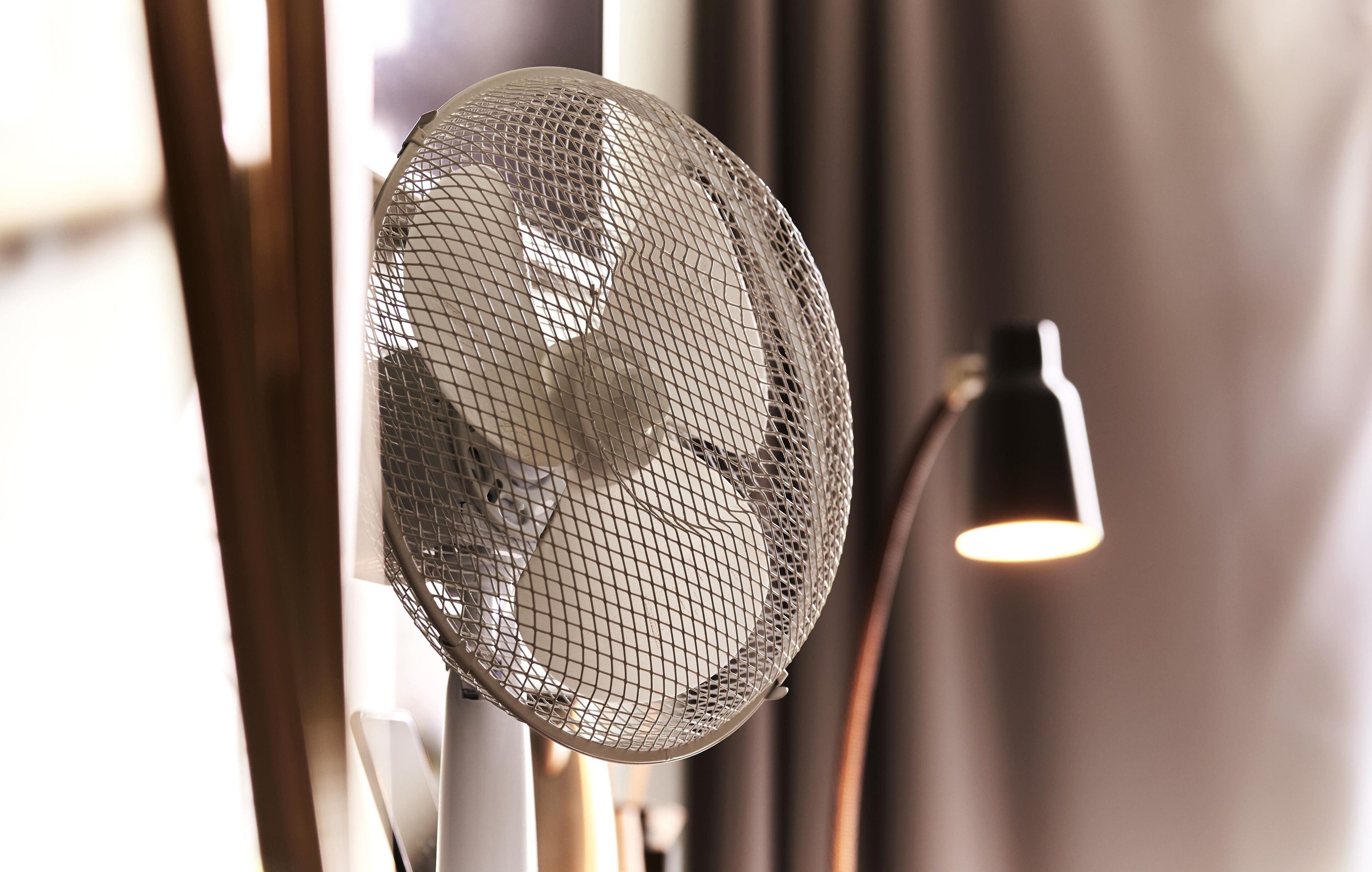 Una habitación con ventilador de pie, lámpara y ventana con cortinas.