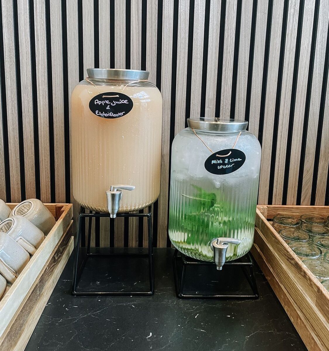 Two beverage dispensers with labels, one for apple juice and one for mint water, against a striped wall.