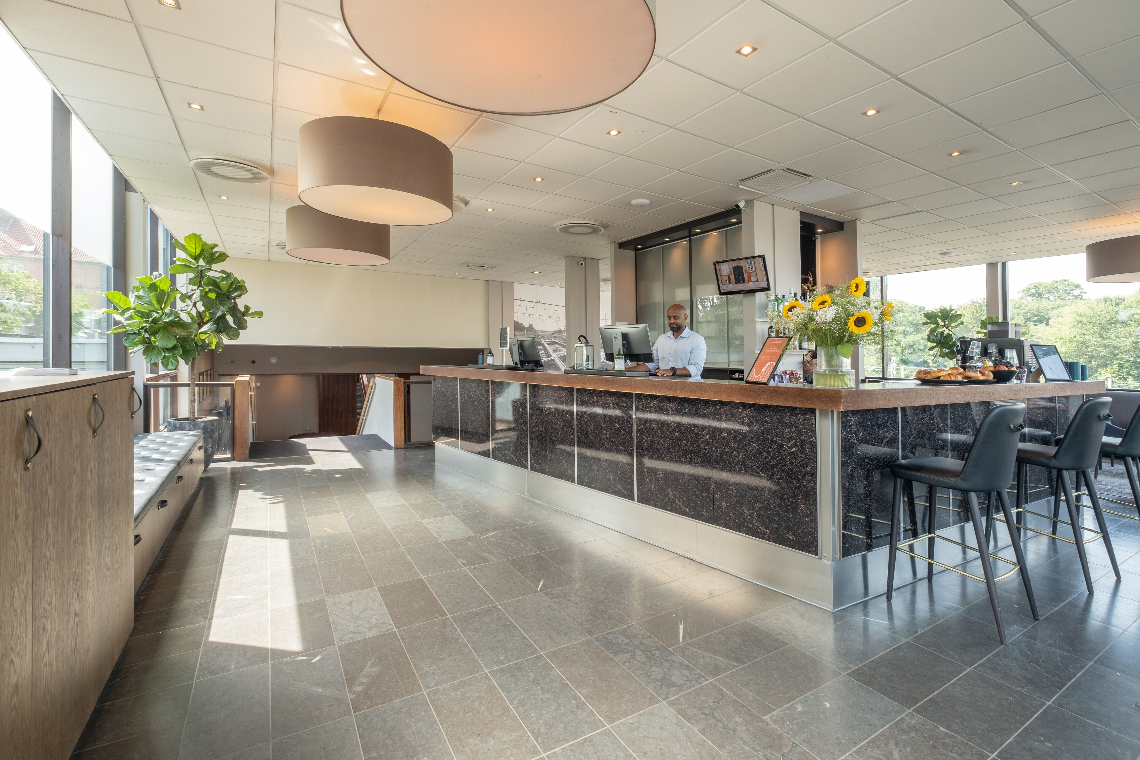 A modern bar area with a marble counter, black bar stools, and a large potted plant.