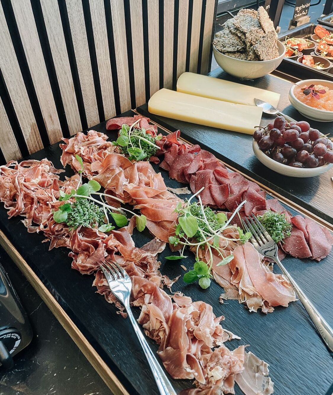Una tabla de fiambres con diferentes carnes y quesos, acompañada de uvas y galletas.