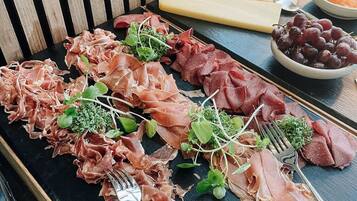 Una tabla de fiambres con diferentes carnes y quesos, acompañada de uvas y galletas.