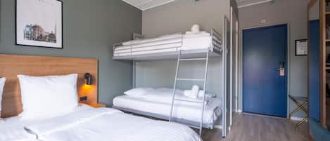 A hotel room with a bunk bed, a single bed, a wooden headboard, a framed cityscape picture, and a blue door.