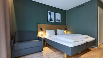 A bedroom with a bed, a chair, two wall-mounted lamps, and two framed pictures on the wall.