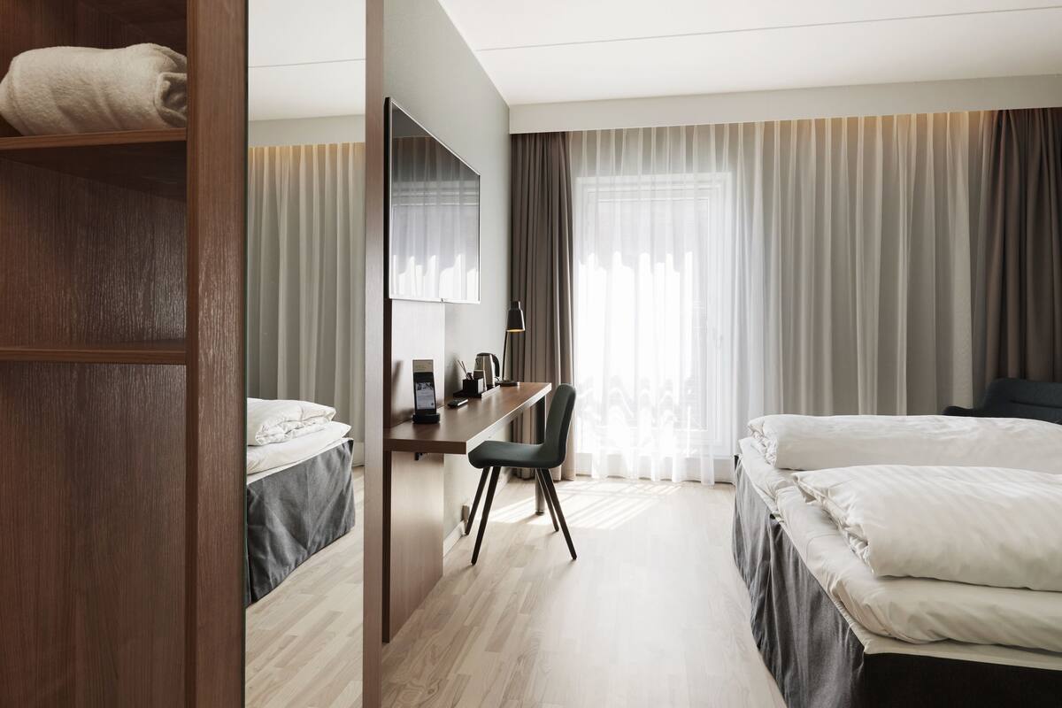 Et hotelværelse med en træskab, et skrivebord med stol, en seng og et stort spejl.
