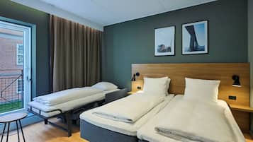 Habitación de hotel con dos camas, una mesita, un balcón con cortinas y dos cuadros en la pared.