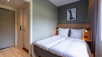 A neatly made bed with white linens in a room with light green walls, a wooden headboard, and a framed picture on the wall.