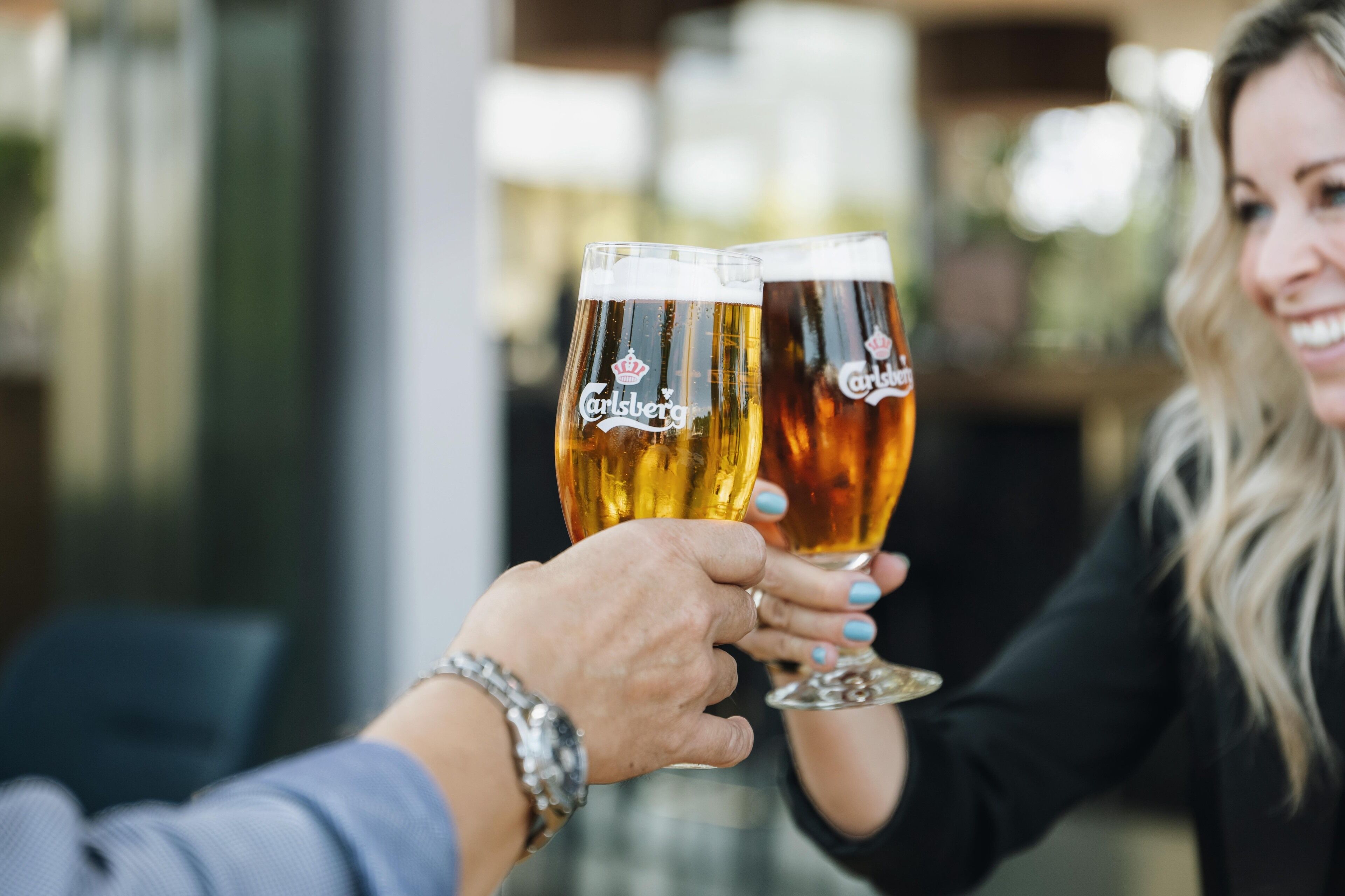 Two people holding glasses of beer with the Carlsberg logo.