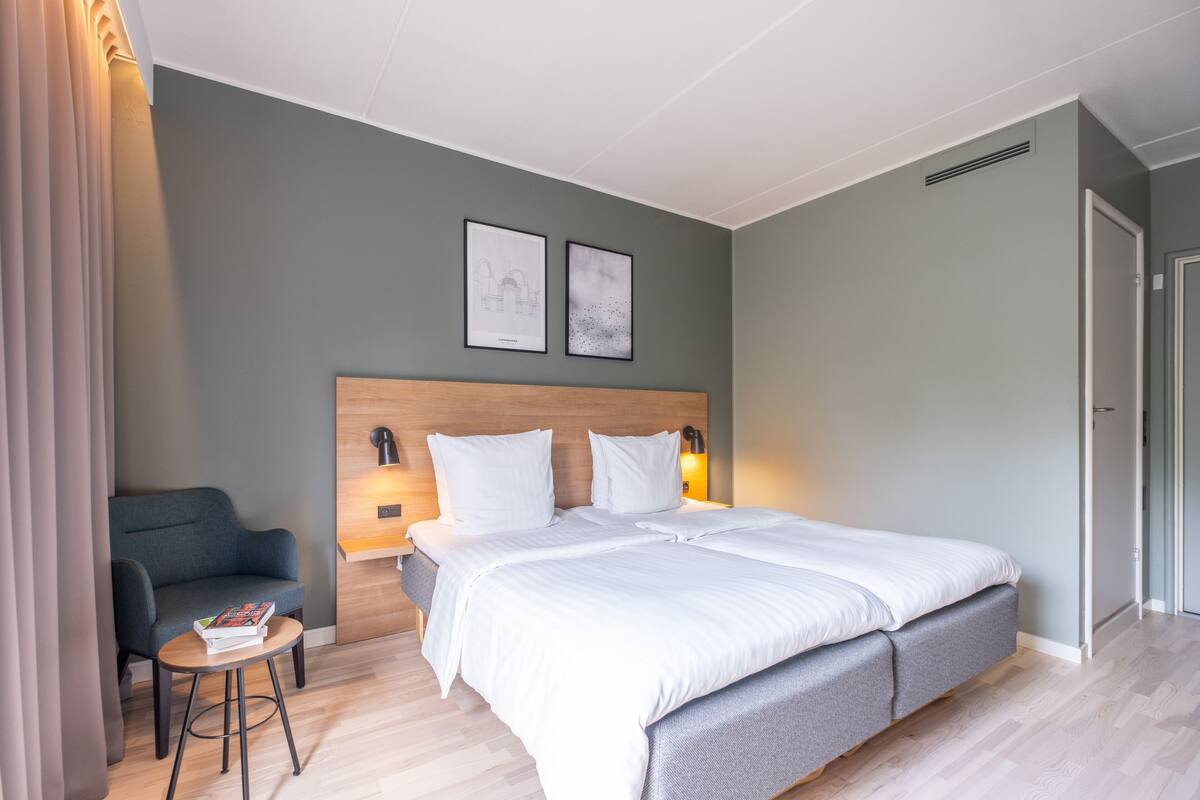 Et moderne hotelværelse med en stor seng, et lille natbord, en stol og to billeder hængende på væggen.