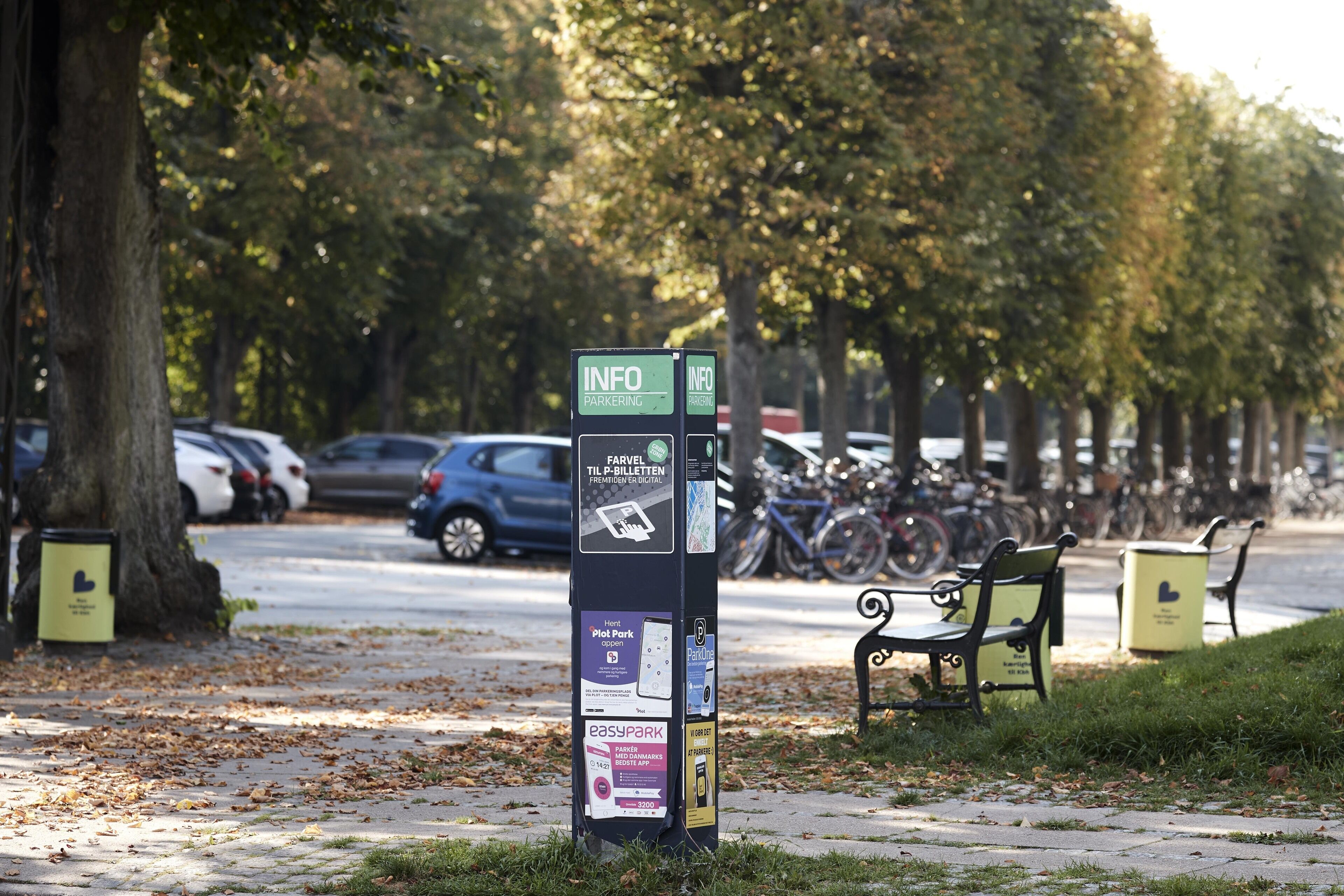 Quiosco de información sobre estacionamiento con varios letreros y un banco cerca.