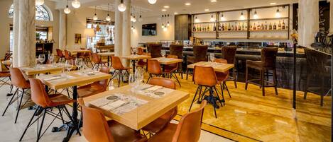 A restaurant with marble flooring, wooden tables, and orange chairs.