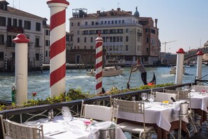 A waterfront restaurant with tables set for dining, a canal with boats, and historic buildings in the background. - CHC Continental, BW Premier Collection (Venice)