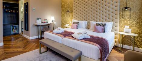 A hotel room with a large bed, a bench, a bedside table, a lamp, and a wardrobe.