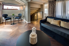 A modern living room with a dark sofa, a coffee table, and a dining area with chairs and a table.