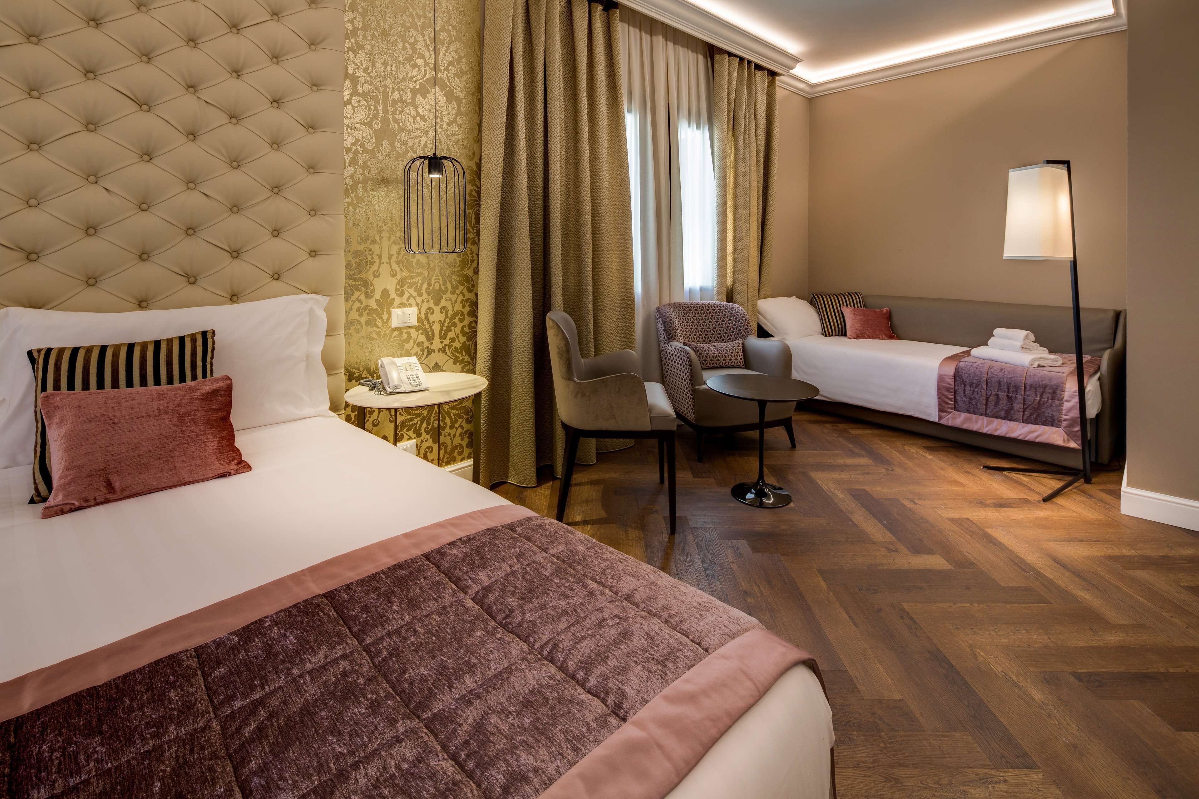 Una habitación de hotel con una cama grande, un sofá, una silla, una mesita y una lámpara.