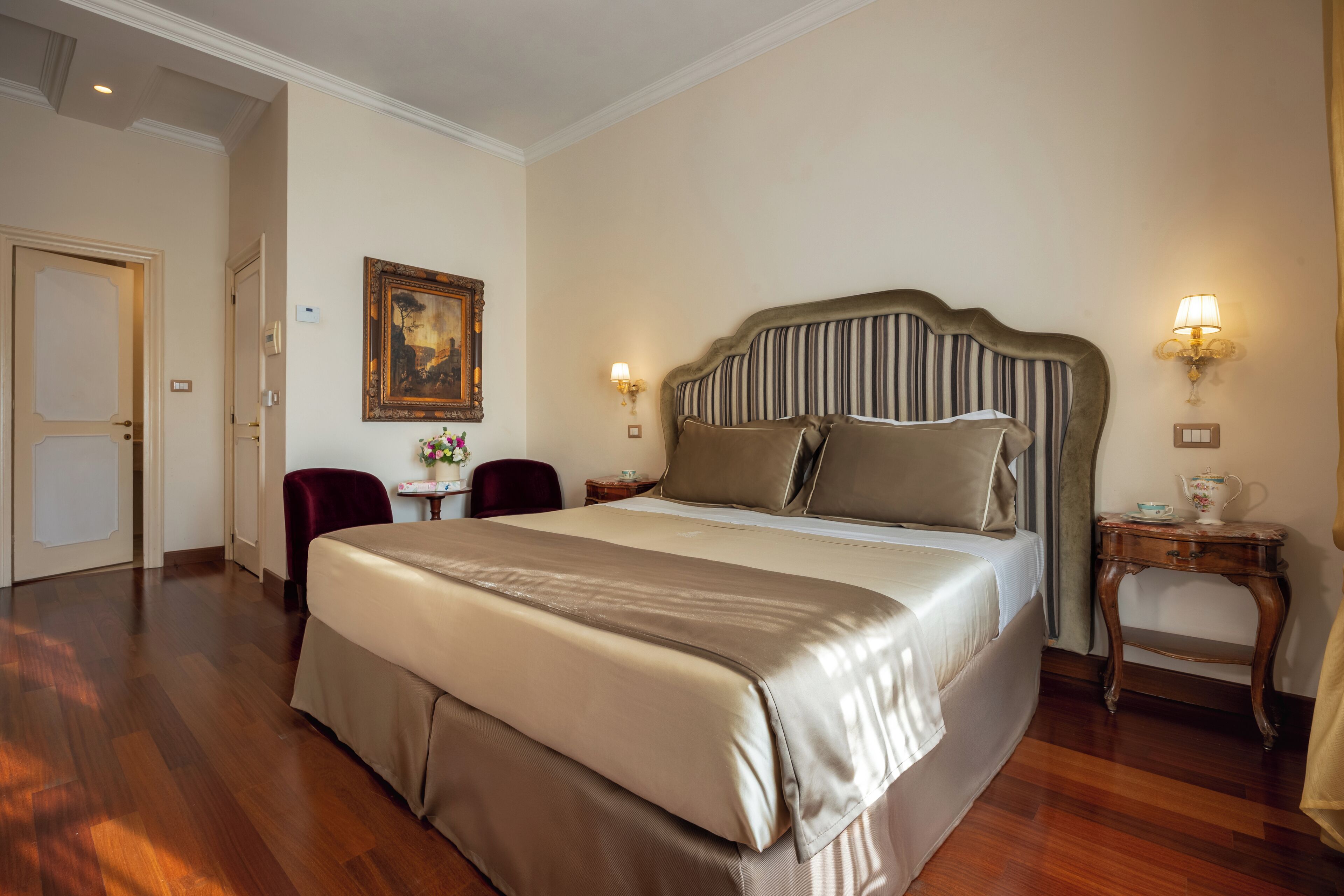 Una cama grande con cabecera a rayas, una mesita con lámpara y un cuadro en la pared.