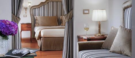 A hotel room with a bed, a sofa, a nightstand with a lamp, a vase with flowers, and a window with curtains.