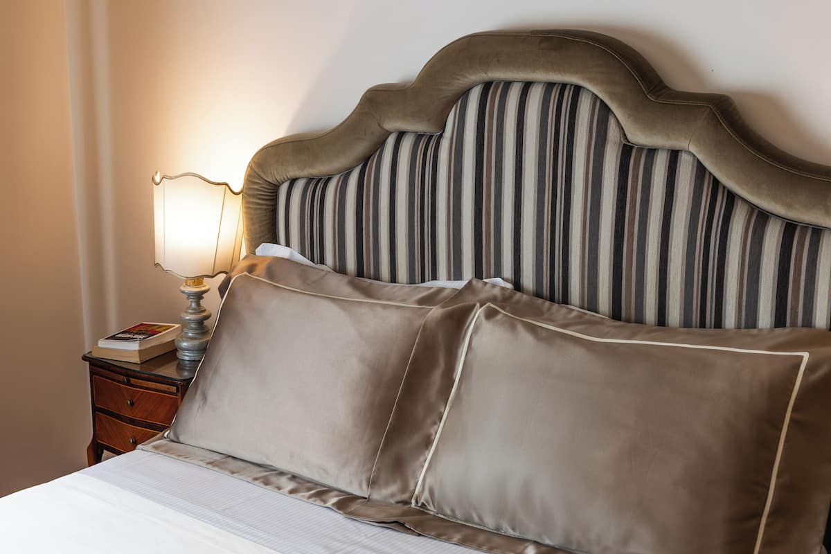 A neatly made bed with a striped headboard, a bedside lamp, and a book on the nightstand.