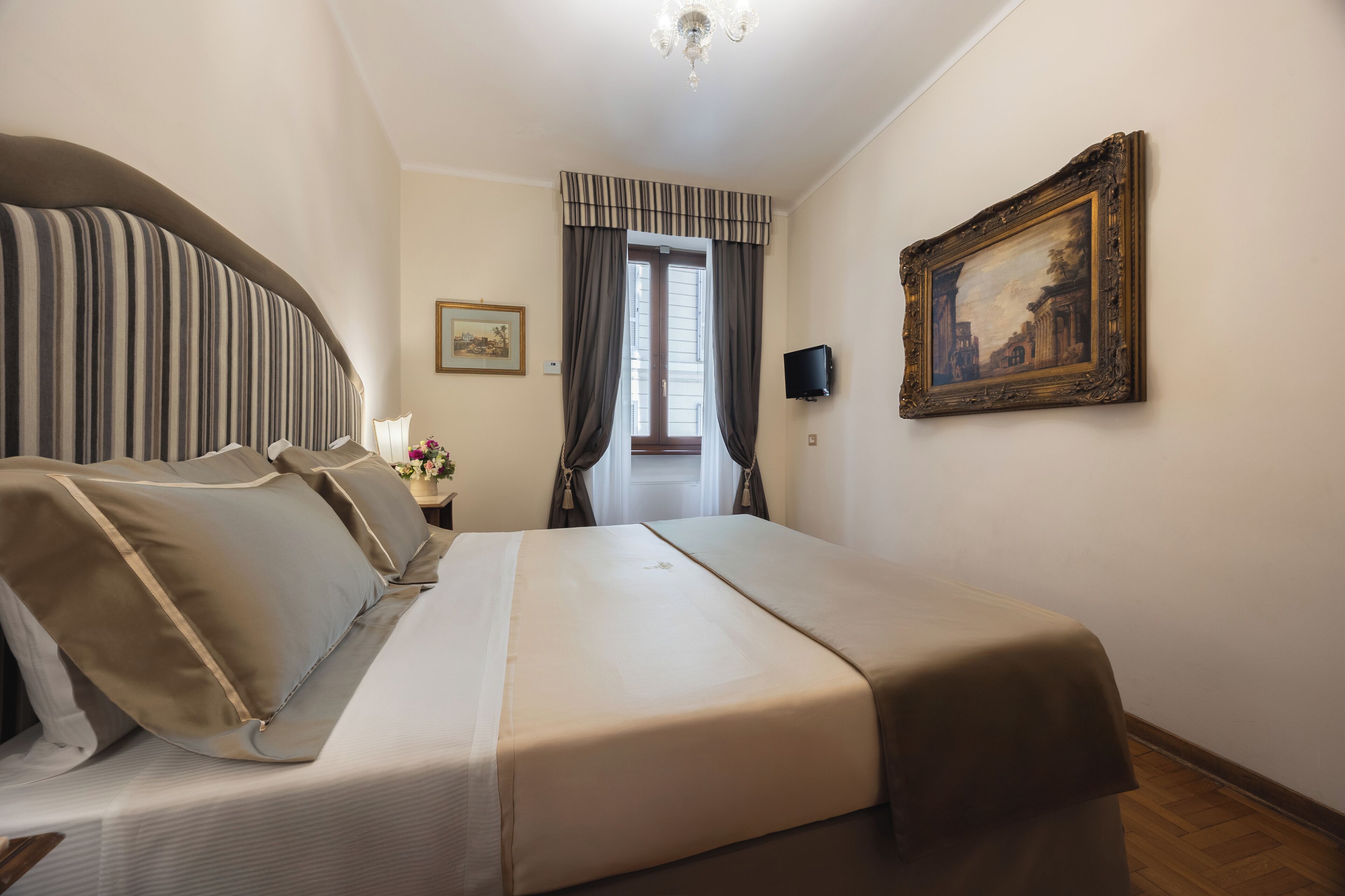 Une chambre d’hôtel avec un grand lit, une télévision, un tableau et une fenêtre avec des rideaux.