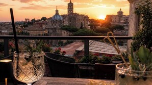 Una mesa con bebidas, aperitivos y vista a un paisaje urbano al atardecer.