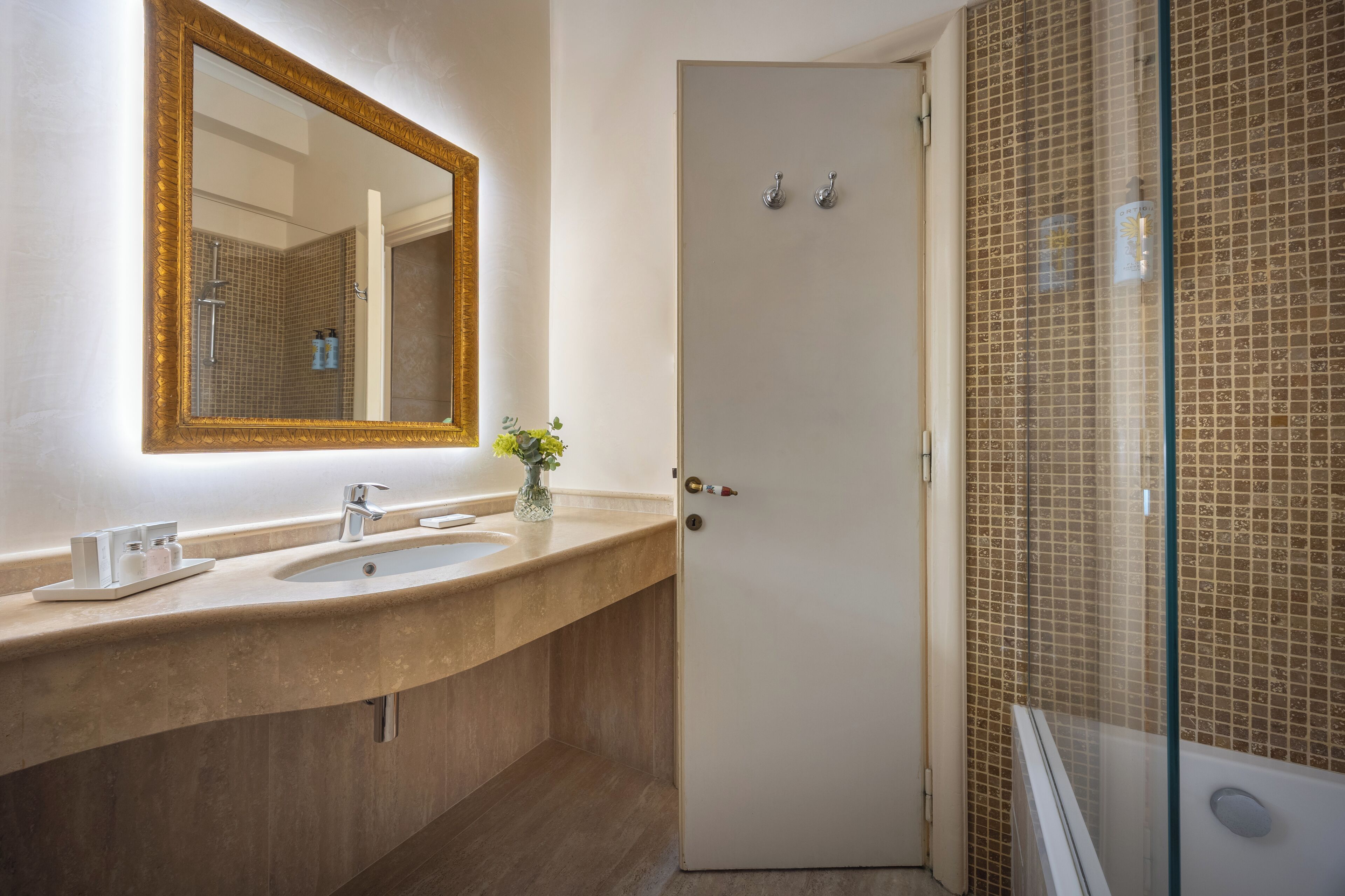 A bathroom with a large mirror, two sinks, a vase with flowers, and a shower area with a glass door.