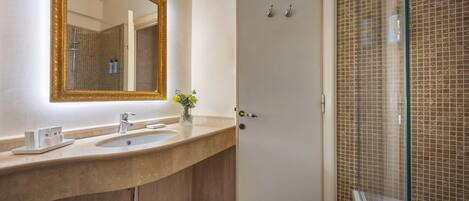 A bathroom with a large mirror, two sinks, a vase with flowers, and a shower area with a glass door.