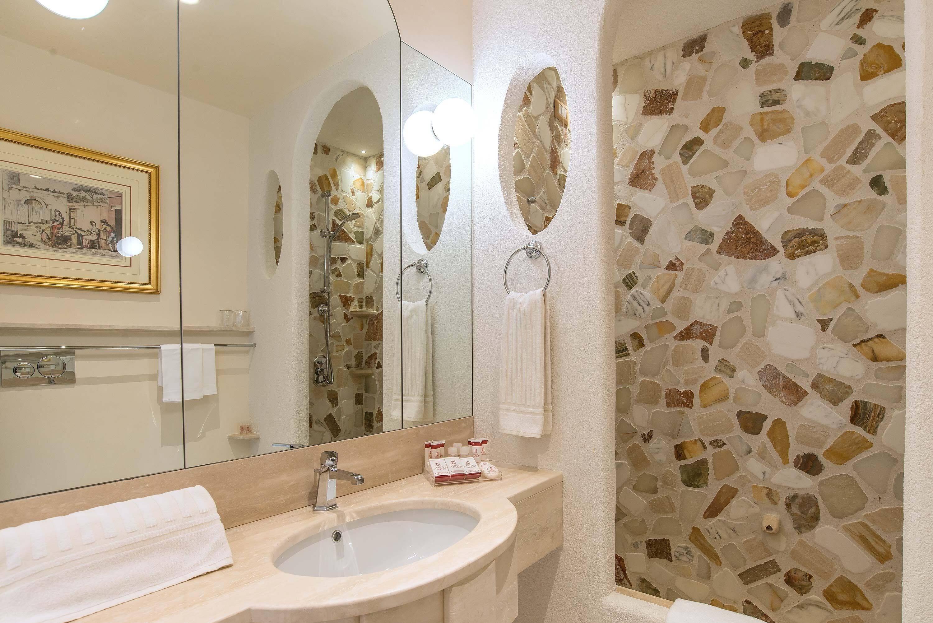 Une salle de bain avec un mur décoré d’une mosaïque de pierre, un lavabo avec un miroir et un tableau encadré accroché au mur.