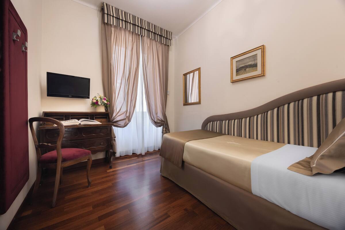 A hotel room with a bed, a desk with a chair, a television, and curtains.