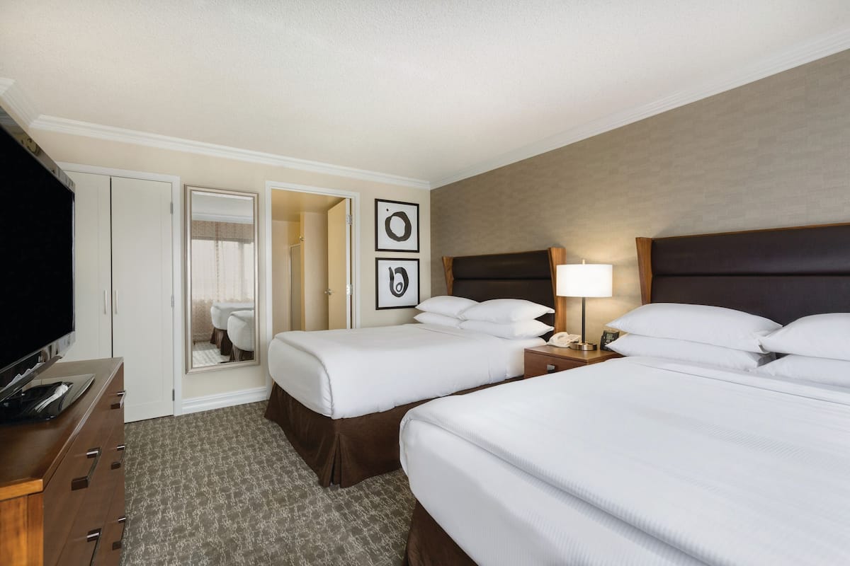 A hotel room with two beds, a TV, a desk, and a mirror.