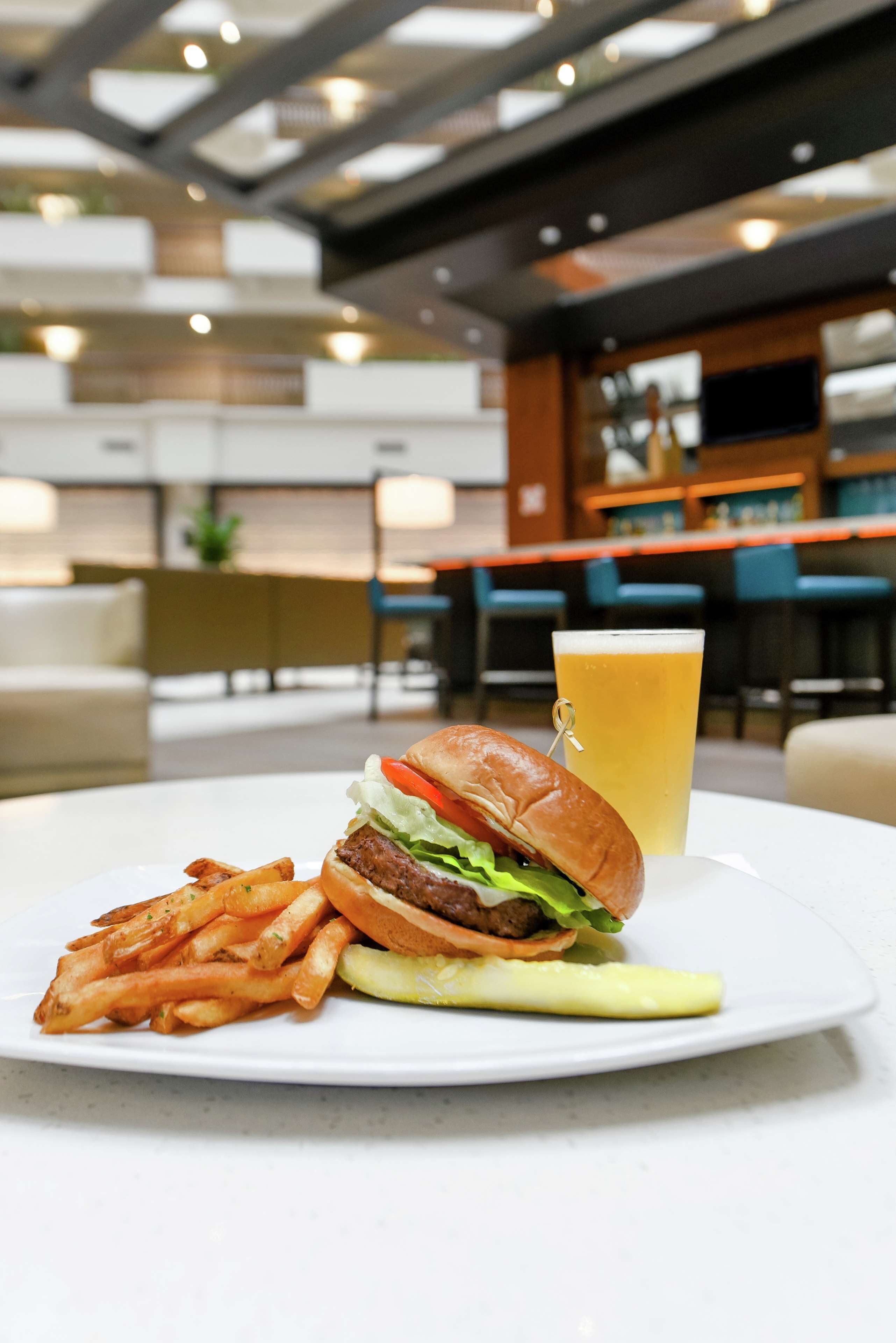 A meal with a burger, fries, and a pickle on a plate, with a glass of beer in the background.