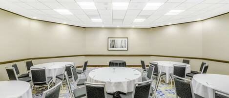 Un salón de conferencias con mesas redondas, sillas y un cuadro en la pared.