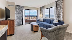 Une chambre d’hôtel moderne dotée d’une grande fenêtre, d’un canapé, d’un fauteuil, d’une télévision et d’une petite table ronde.