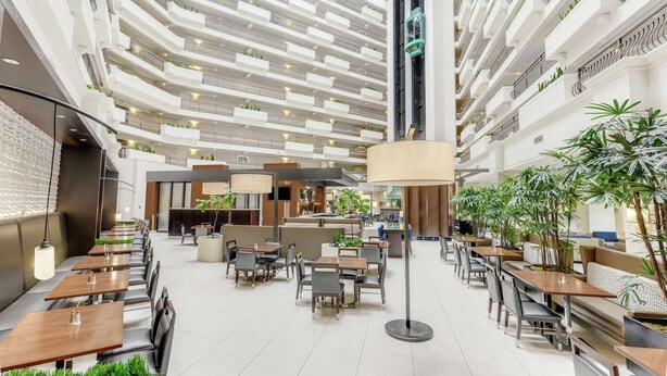 Un atrium d’hôtel moderne doté de plusieurs espaces de restauration, de hauts plafonds et de plantes d’intérieur.