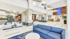 Un hall d’entrée spacieux avec un canapé bleu, des fauteuils blancs et un comptoir d’accueil.