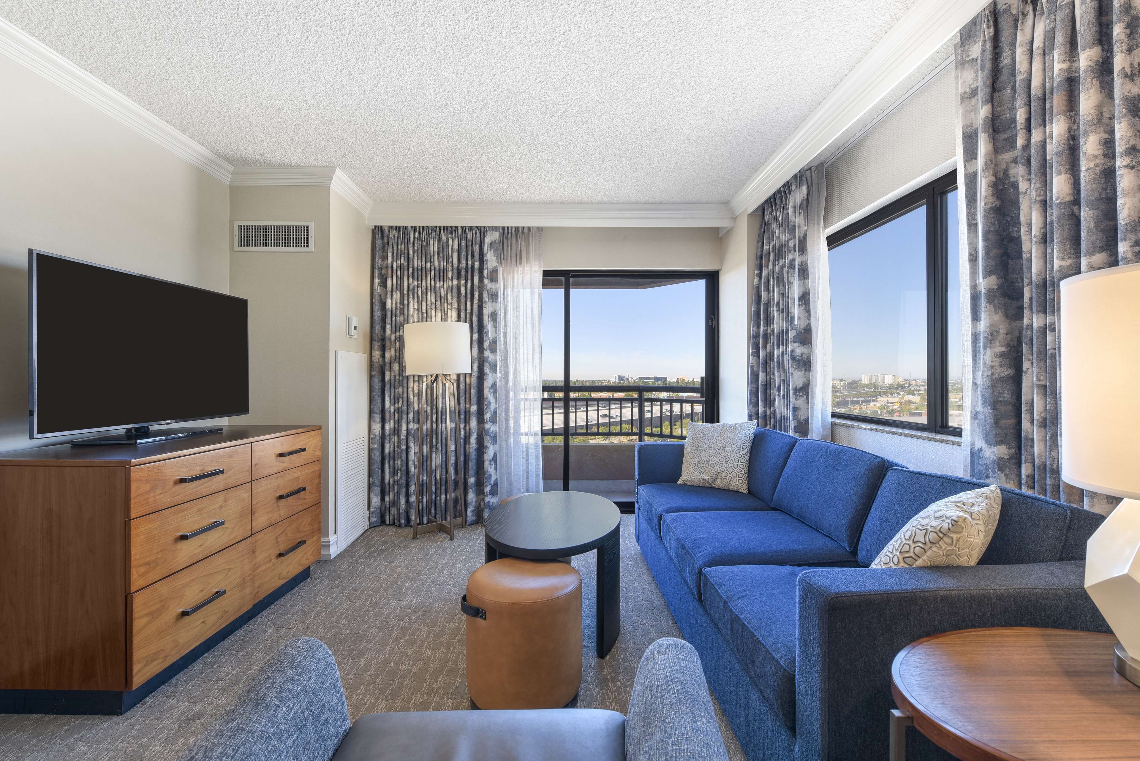 Ein modernes Hotelzimmer mit Flachbildfernseher, einer Couch, einem kleinen Tisch und Blick auf die Stadt.