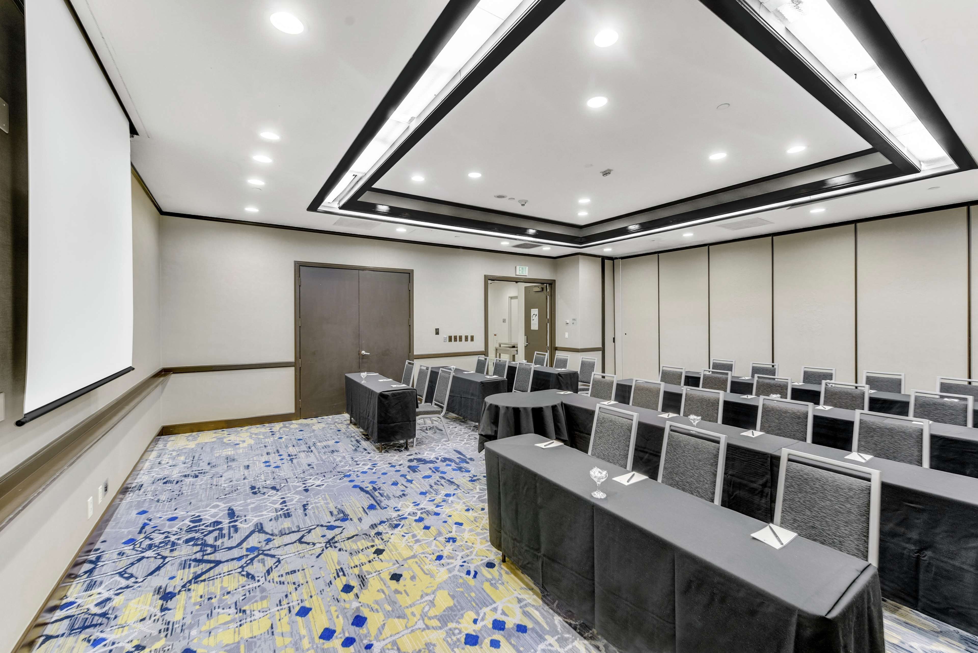 A conference room with rows of tables, a carpeted floor, and a ceiling with recessed lighting.