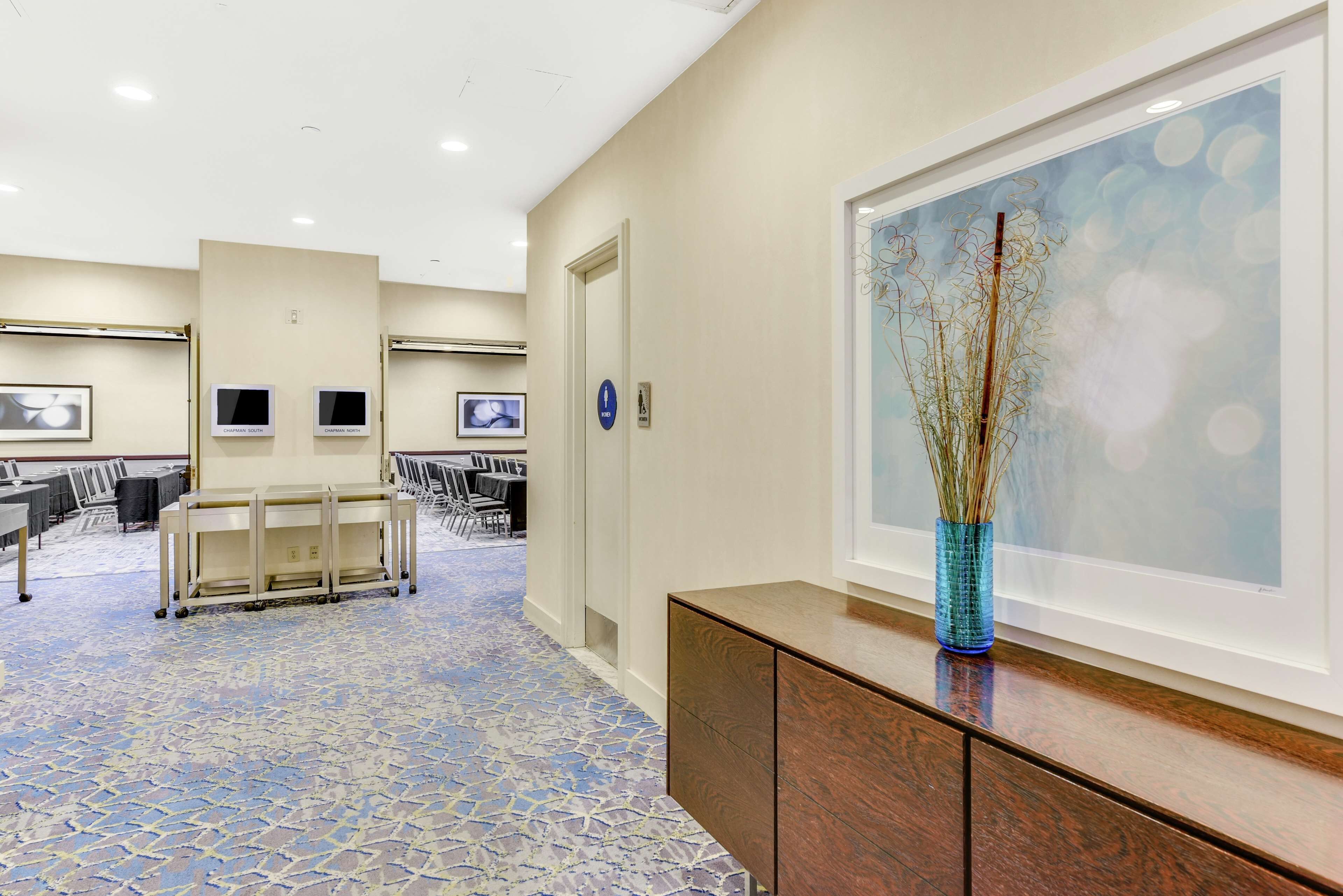 A hotel lobby with a patterned carpet, a reception desk, a wall-mounted TV, and a framed artwork.