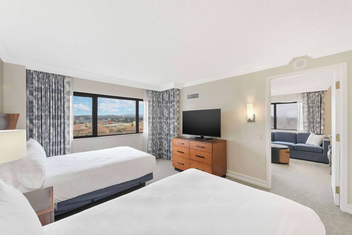 A hotel room with two beds, a television, and a view of the city.