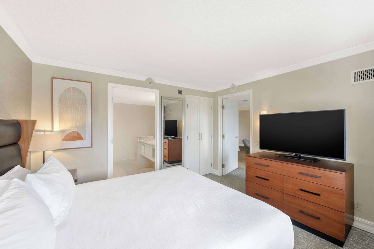 A hotel room with a bed, a TV on a dresser, and a door leading to another room.